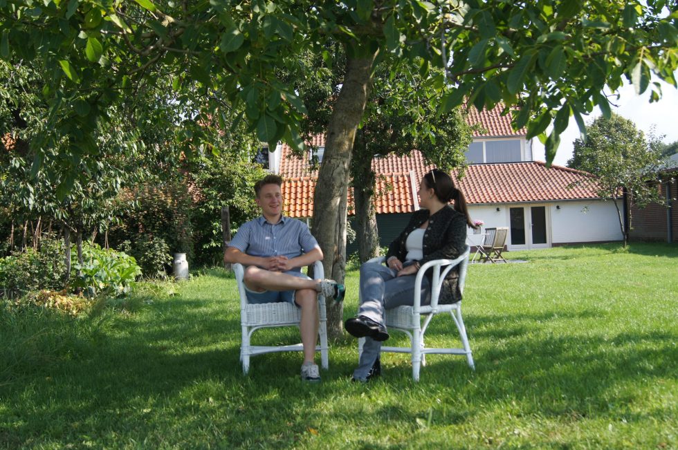 Twee vrienden zitten op een stoel onder een boom op Hoeve Linnerveld